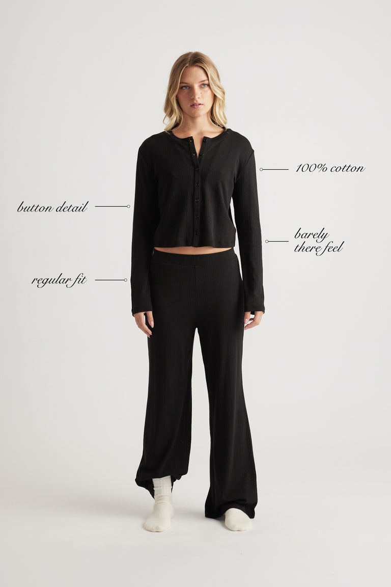 Woman wearing black button-up sleep top with long sleeves in soft cotton fabric and relaxed fit paired with matching pants