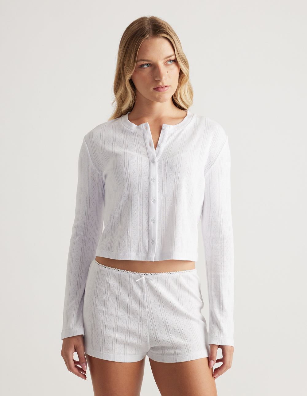 Woman wearing soft white pointelle knit button-up top with long sleeves and relaxed fit paired with matching shorts