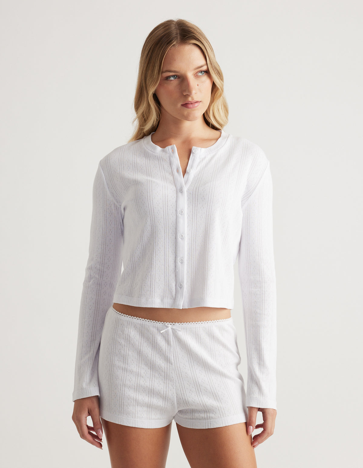 Woman wearing soft white pointelle knit button-up top with long sleeves and relaxed fit paired with matching shorts