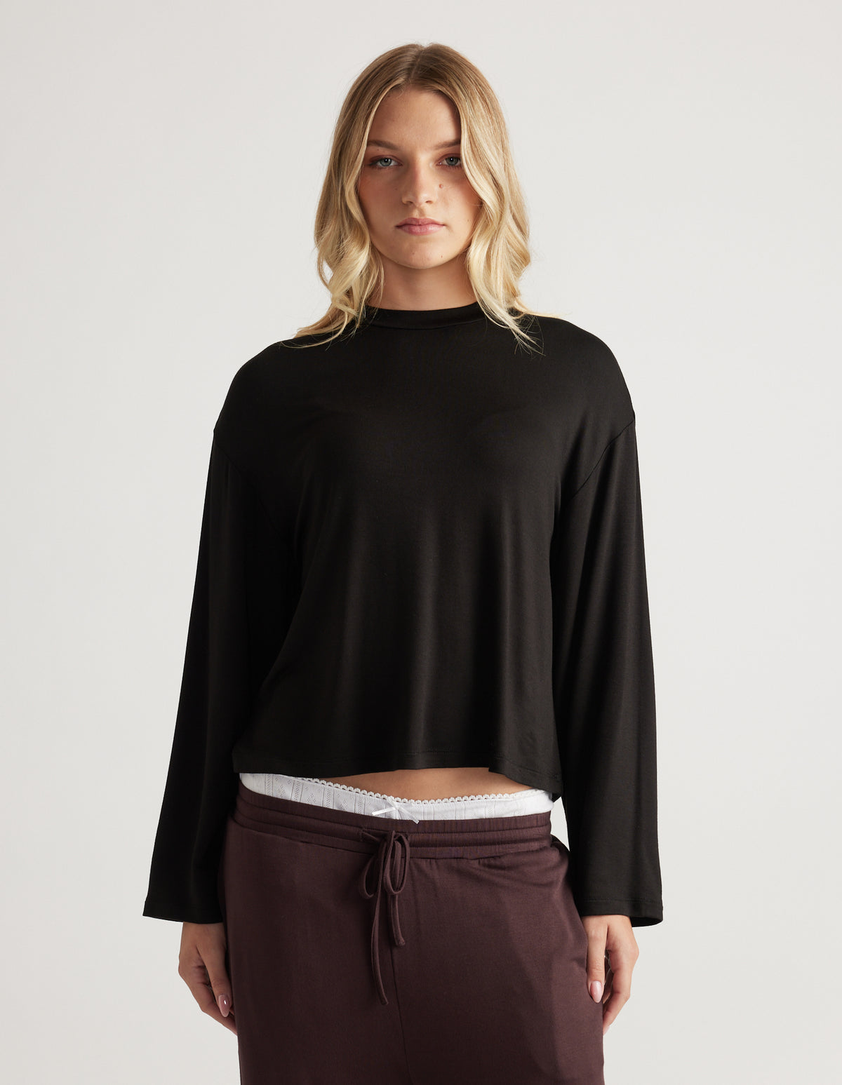 Woman modeling a relaxed black long sleeve sleep top with a soft drape paired with deep plum drawstring pants