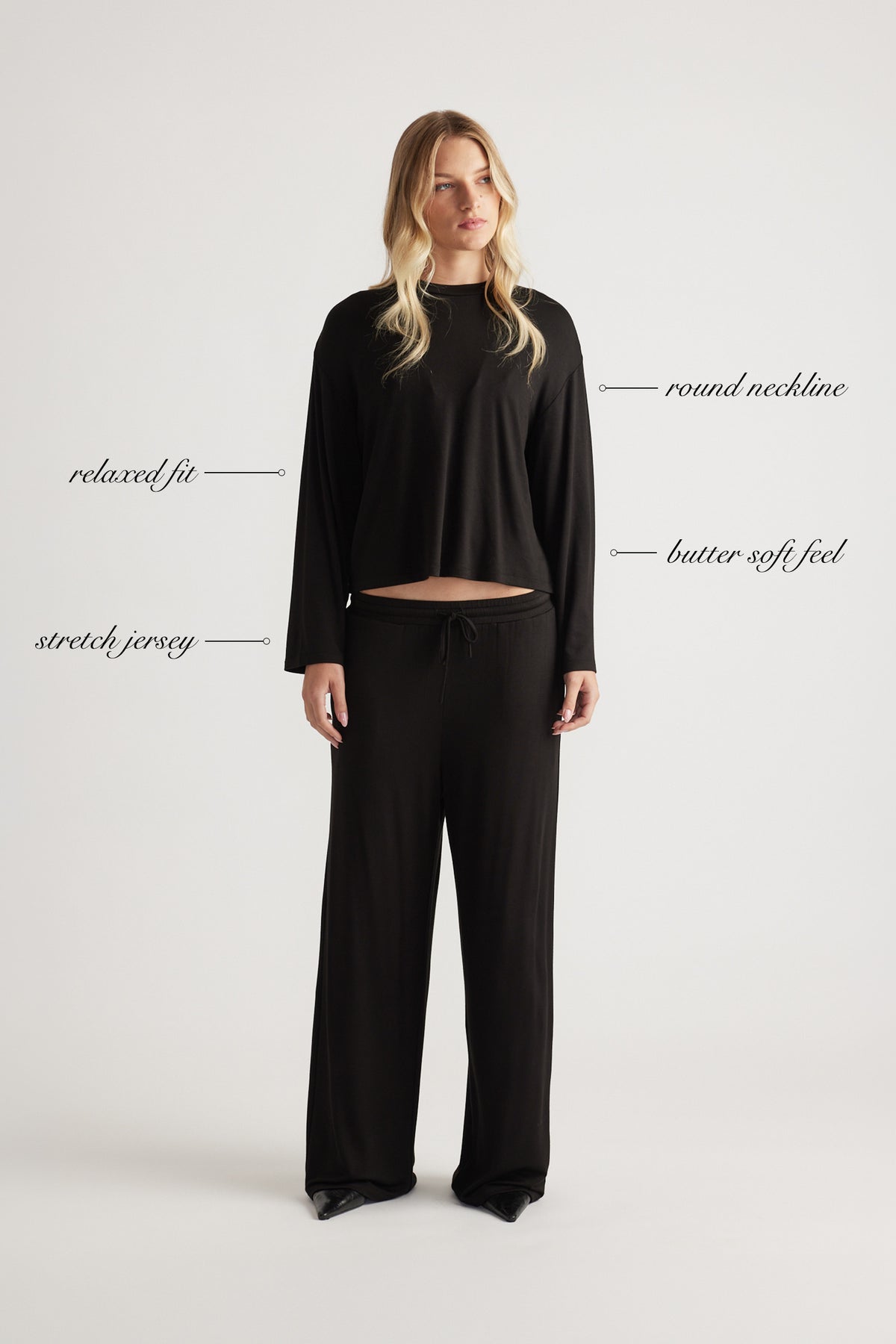 Woman wearing relaxed black sleep jersey top with long sleeves and round neckline paired with matching wide-leg pants