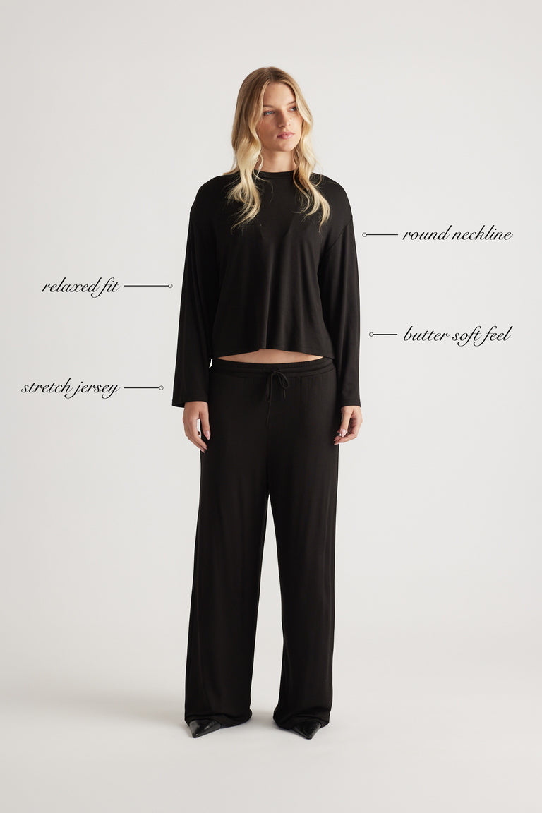 Woman wearing relaxed black sleep jersey top with long sleeves and round neckline paired with matching wide-leg pants
