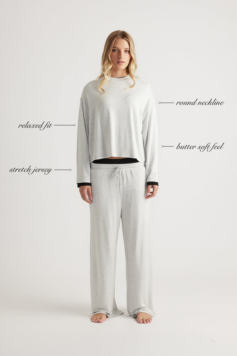 Woman wearing light grey relaxed fit long sleeve sleep jersey top with round neckline and matching pants