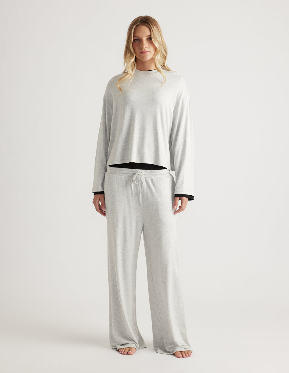 Woman wearing a light grey sleep jersey long sleeve top with matching wide-leg lounge pants against a plain backdrop