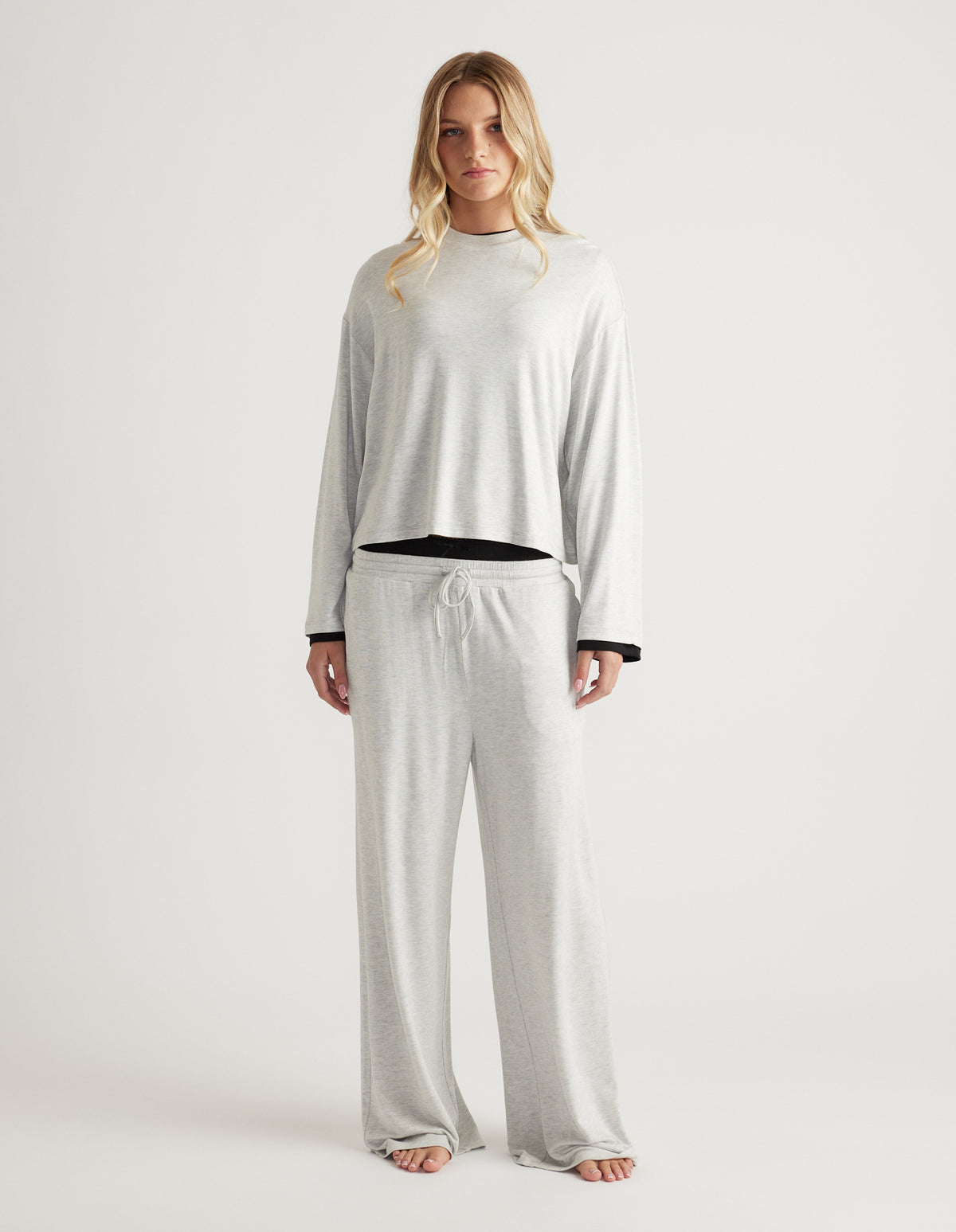 Woman wearing a light grey sleep jersey long sleeve top with matching wide-leg lounge pants against a plain backdrop