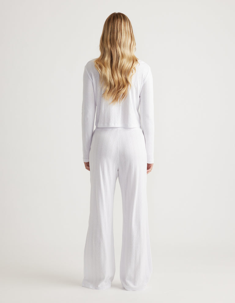 Woman with long wavy blonde hair wearing white wide-leg ribbed pants and matching long-sleeve top viewed from behind