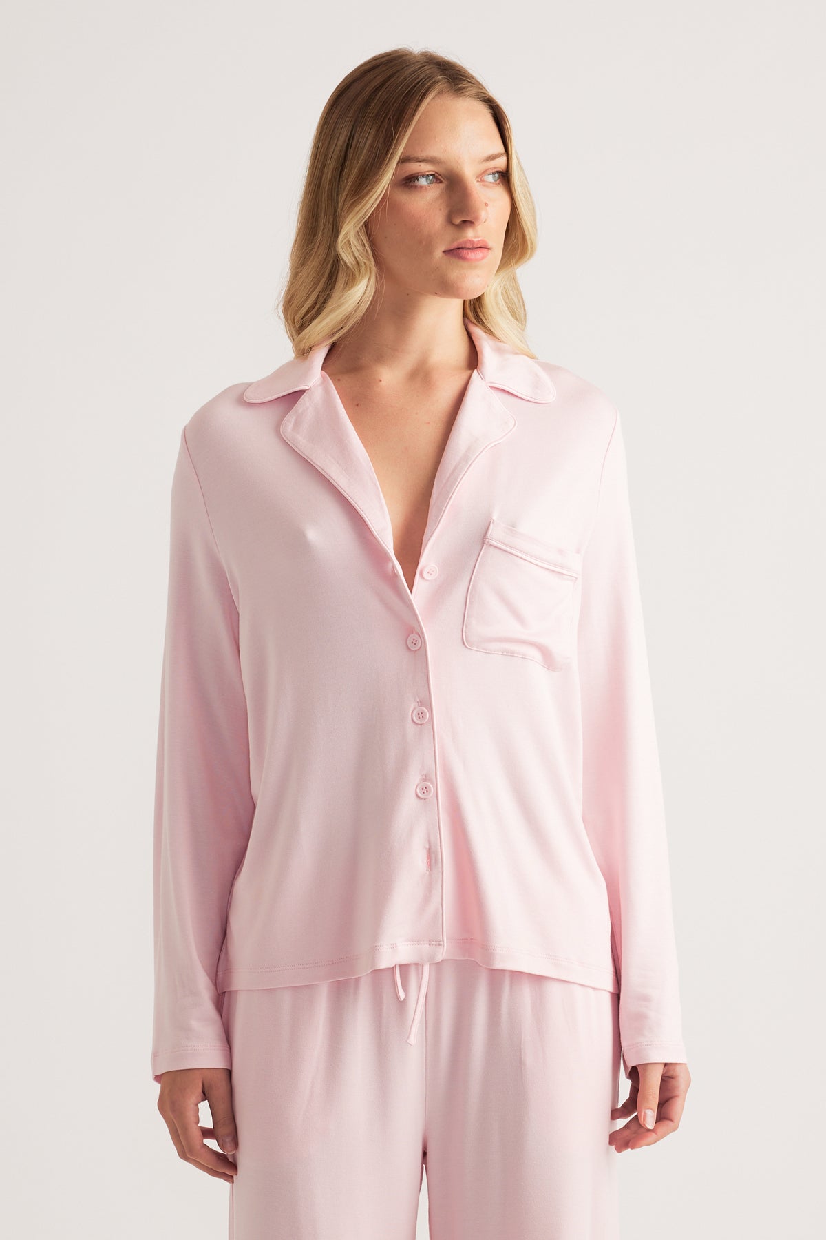 Woman wearing a pale pink button front sleep shirt with a collared neckline and matching drawstring pants