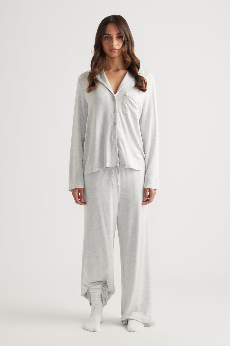 Woman wearing light grey sleep button through shirt with relaxed fit and matching wide leg lounge pants for easy comfort