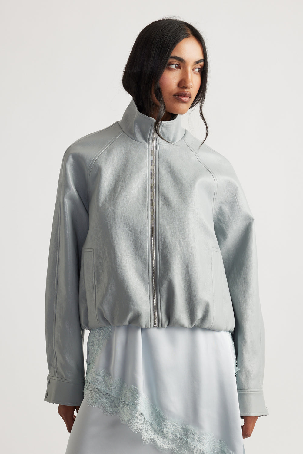 Woman wearing Grace Faux Leather Bomber in soft grey with high collar over lace-trimmed slip dress by DECJUBA Australian brand