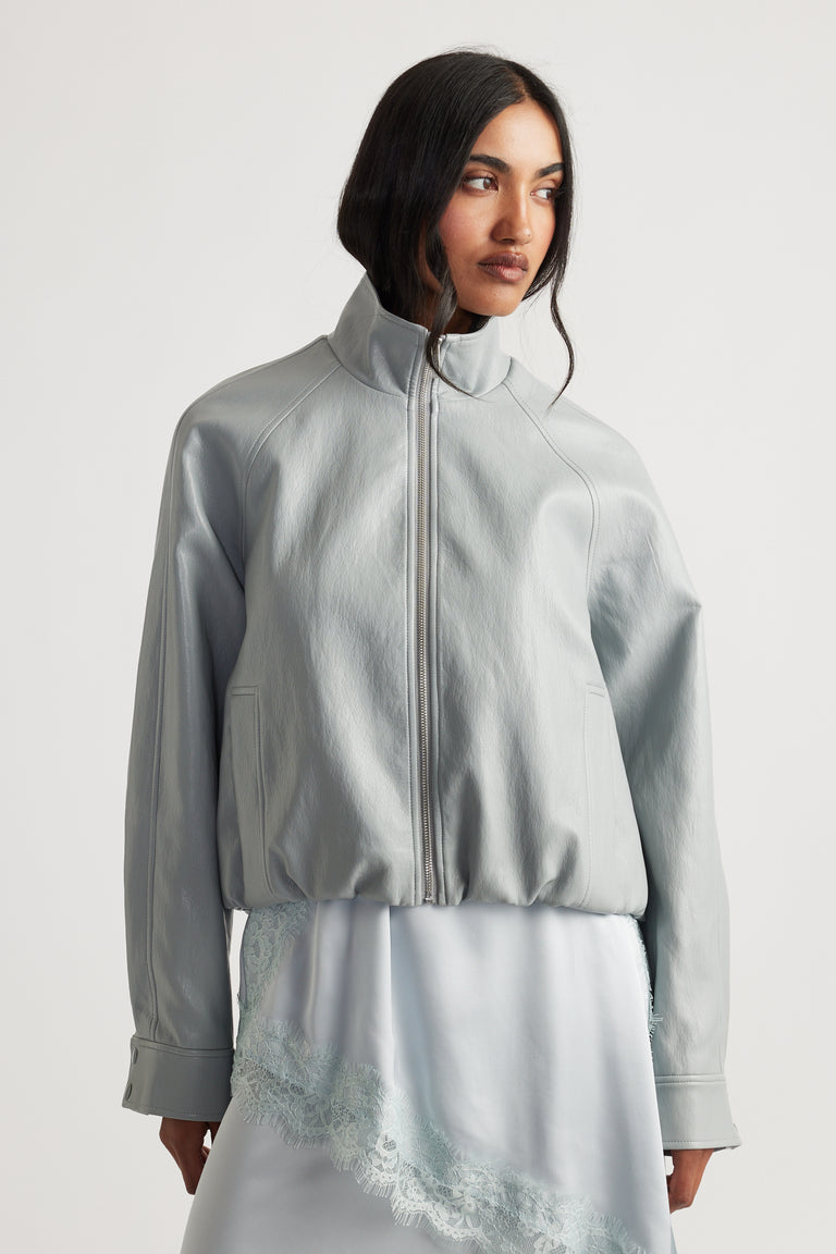 Woman wearing Grace Faux Leather Bomber in soft grey with high collar over lace-trimmed slip dress by DECJUBA Australian brand