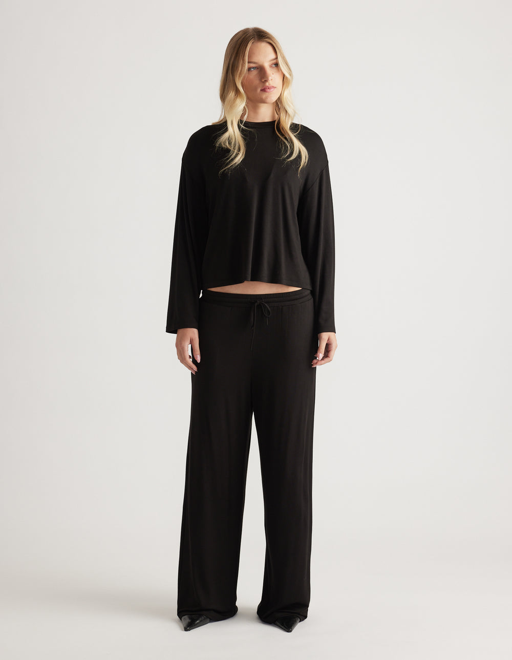 Woman wearing relaxed black wide leg sleep pants with drawstring waist and matching long sleeve top for cozy comfort