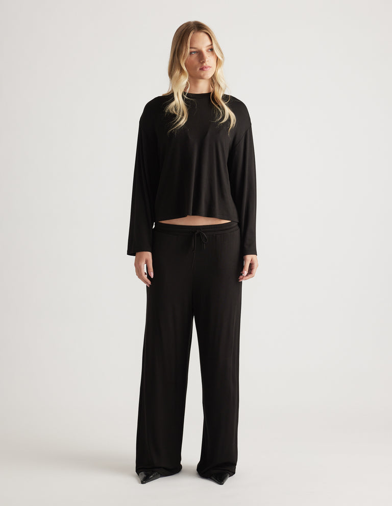 Woman wearing relaxed black wide leg sleep pants with drawstring waist and matching long sleeve top for cozy comfort