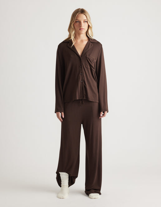 Woman wearing relaxed-fit sleep jersey wide leg pants and matching button-up top in rich chocolate brown