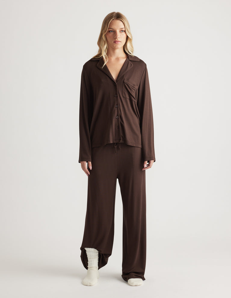 Woman wearing relaxed-fit sleep jersey wide leg pants and matching button-up top in rich chocolate brown
