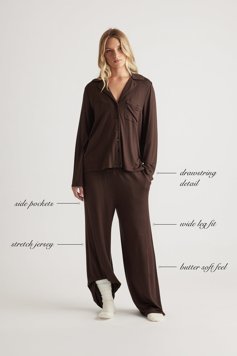 Woman wearing dark chocolate wide-leg sleep jersey pants and matching buttoned top with pockets and drawstring