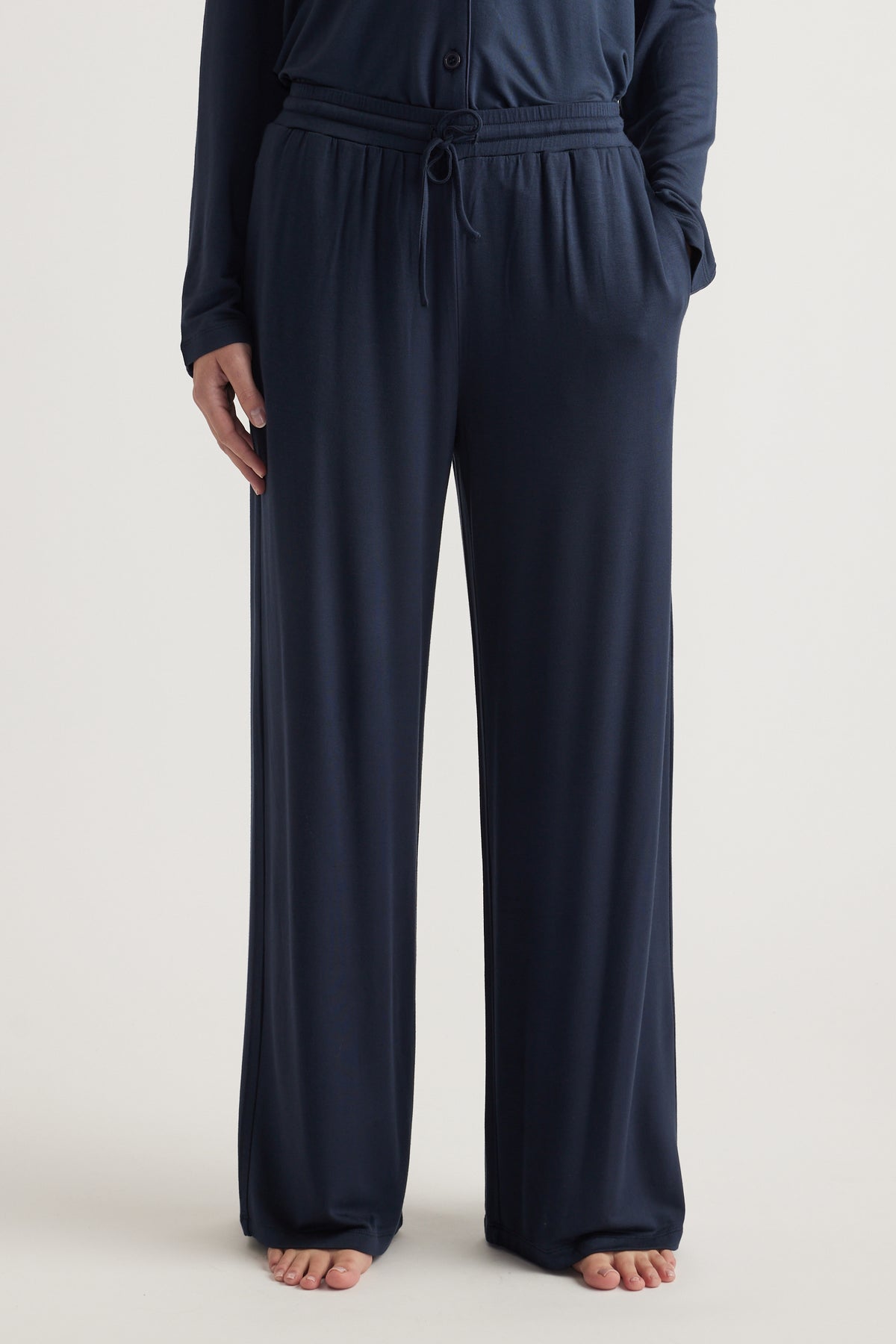 Model wearing navy wide leg jersey pants with an elastic drawstring waist and side pockets