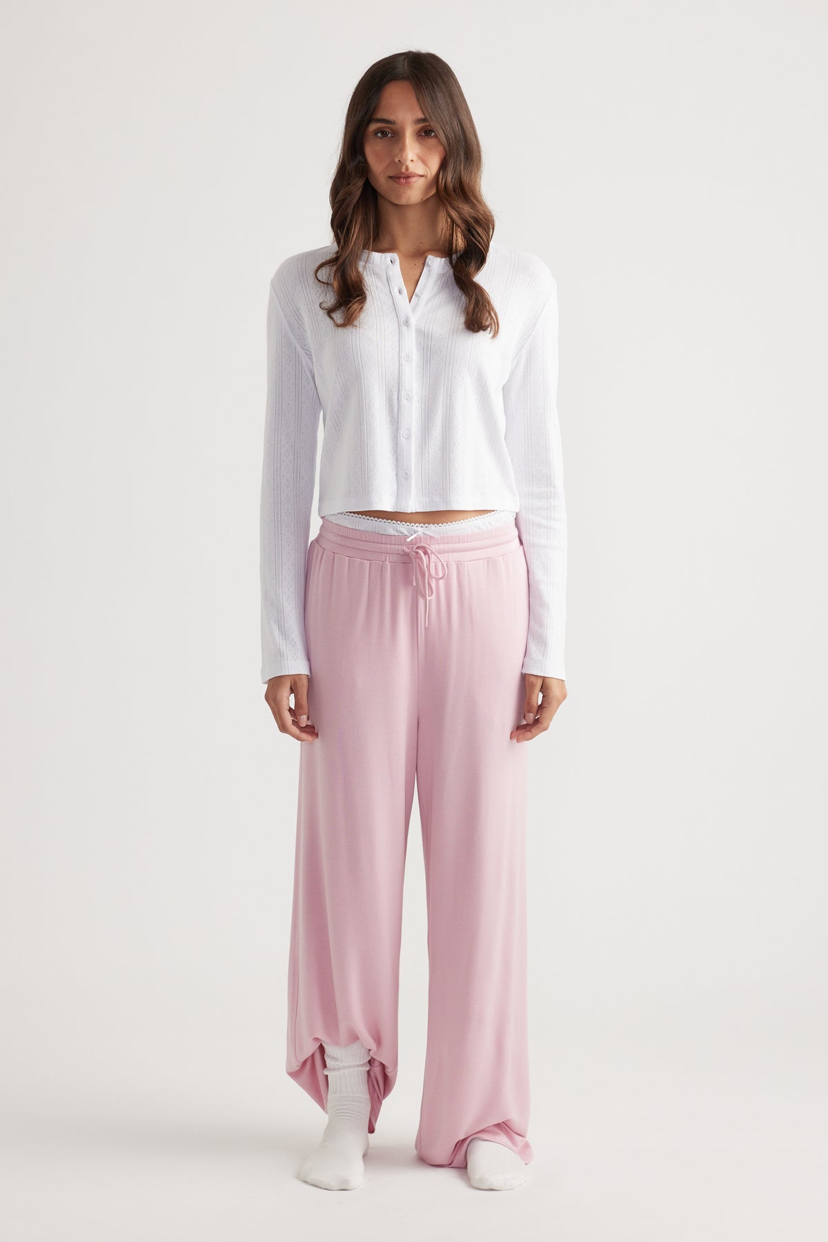 Woman wearing soft pink wide leg pants with drawstring waist paired with a white button-up long sleeve top for relaxed style
