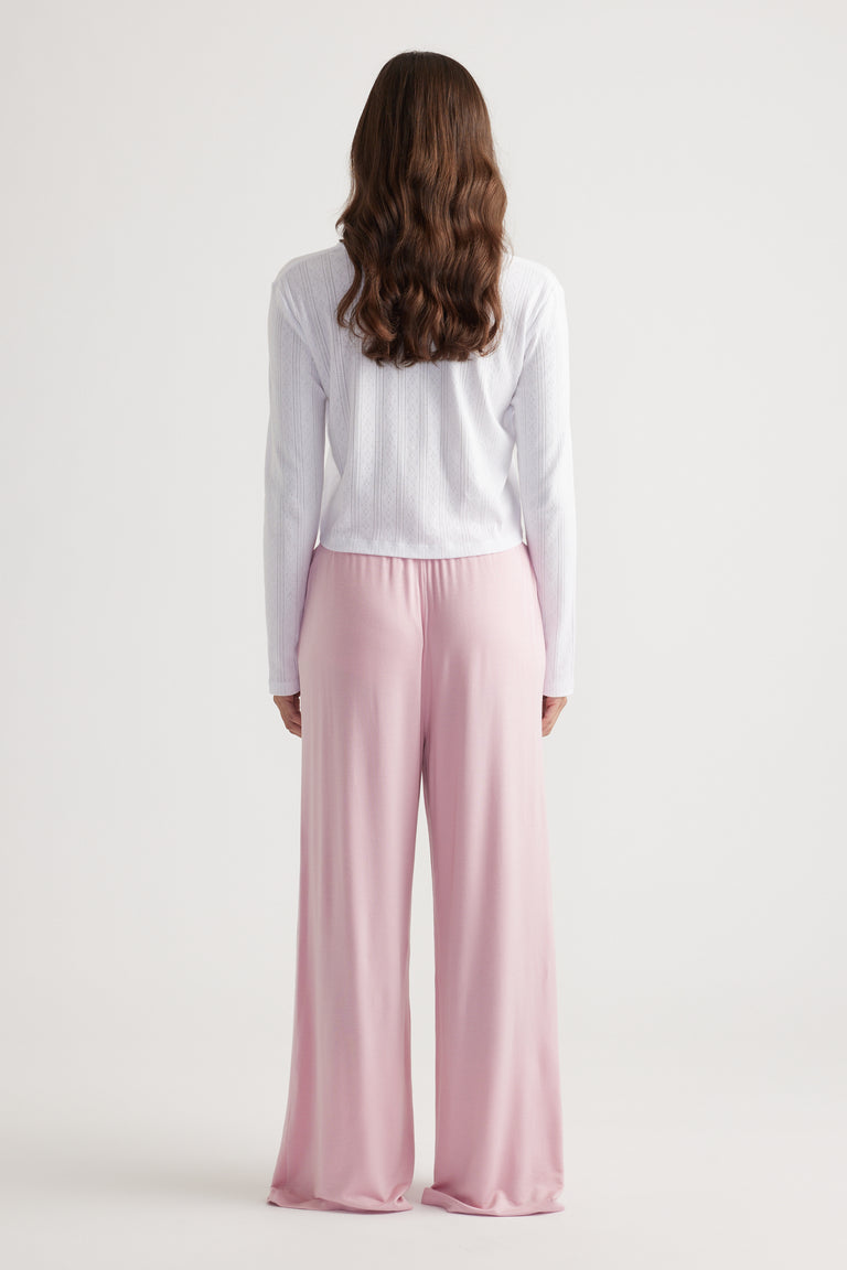 Woman wearing soft pink wide leg sleep jersey pants paired with a white long sleeve top for comfortable loungewear