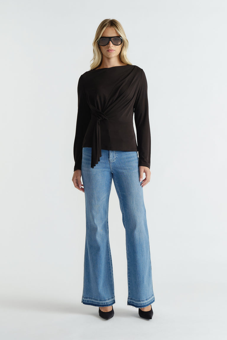 Woman wearing a long-sleeve black top with tie detail paired with light blue wide-leg jeans and black heels