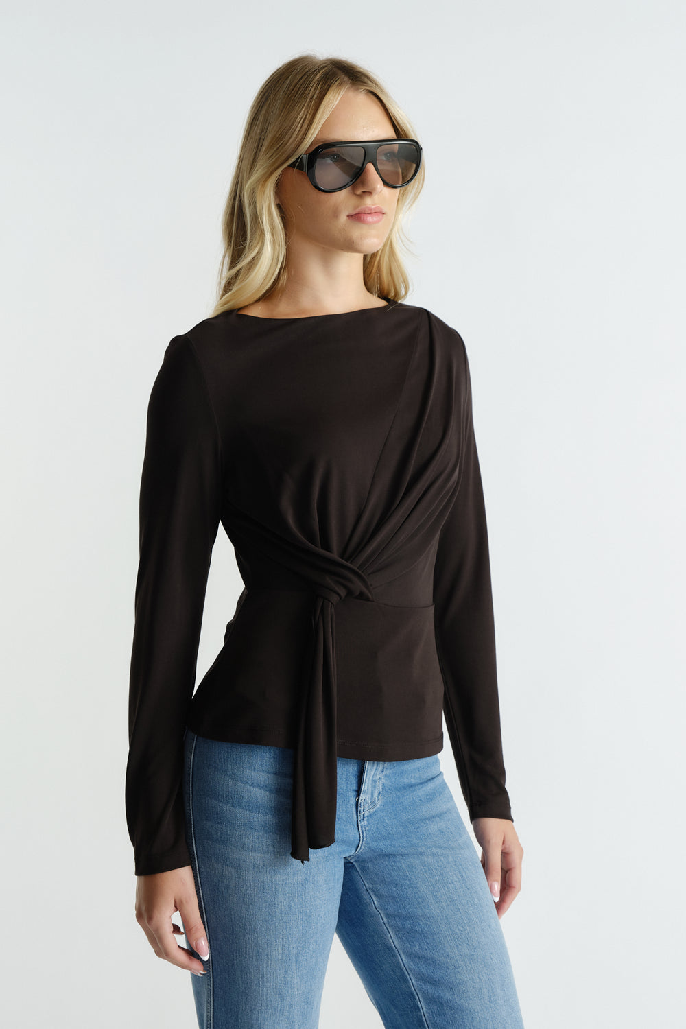 Woman wearing a sleek black long-sleeve top with a tie detail at the waist paired with casual blue jeans
