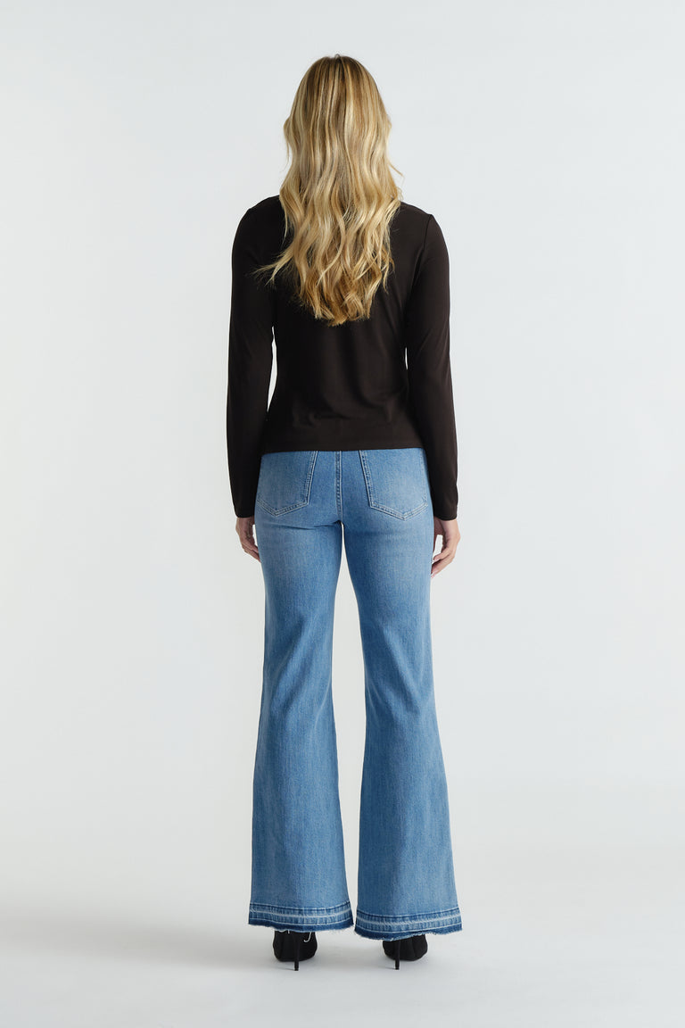 Back view of woman wearing black long-sleeve top paired with high-waisted light blue flared jeans and black heels