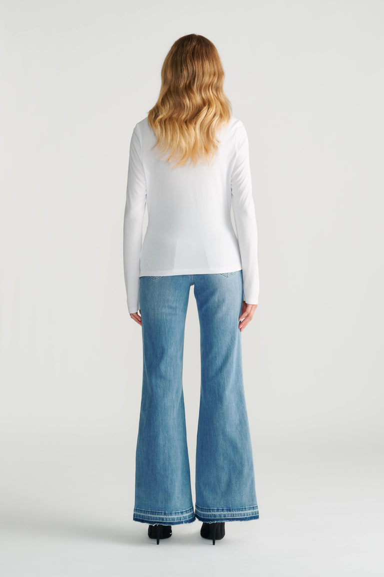 Woman wearing a fitted white long-sleeve top paired with light blue wide-leg denim jeans and black heels, back view.
