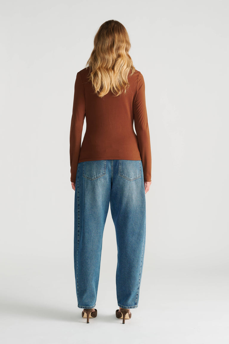 Woman seen from behind wearing a fitted long-sleeve brown top paired with relaxed high-rise blue jeans and heels.