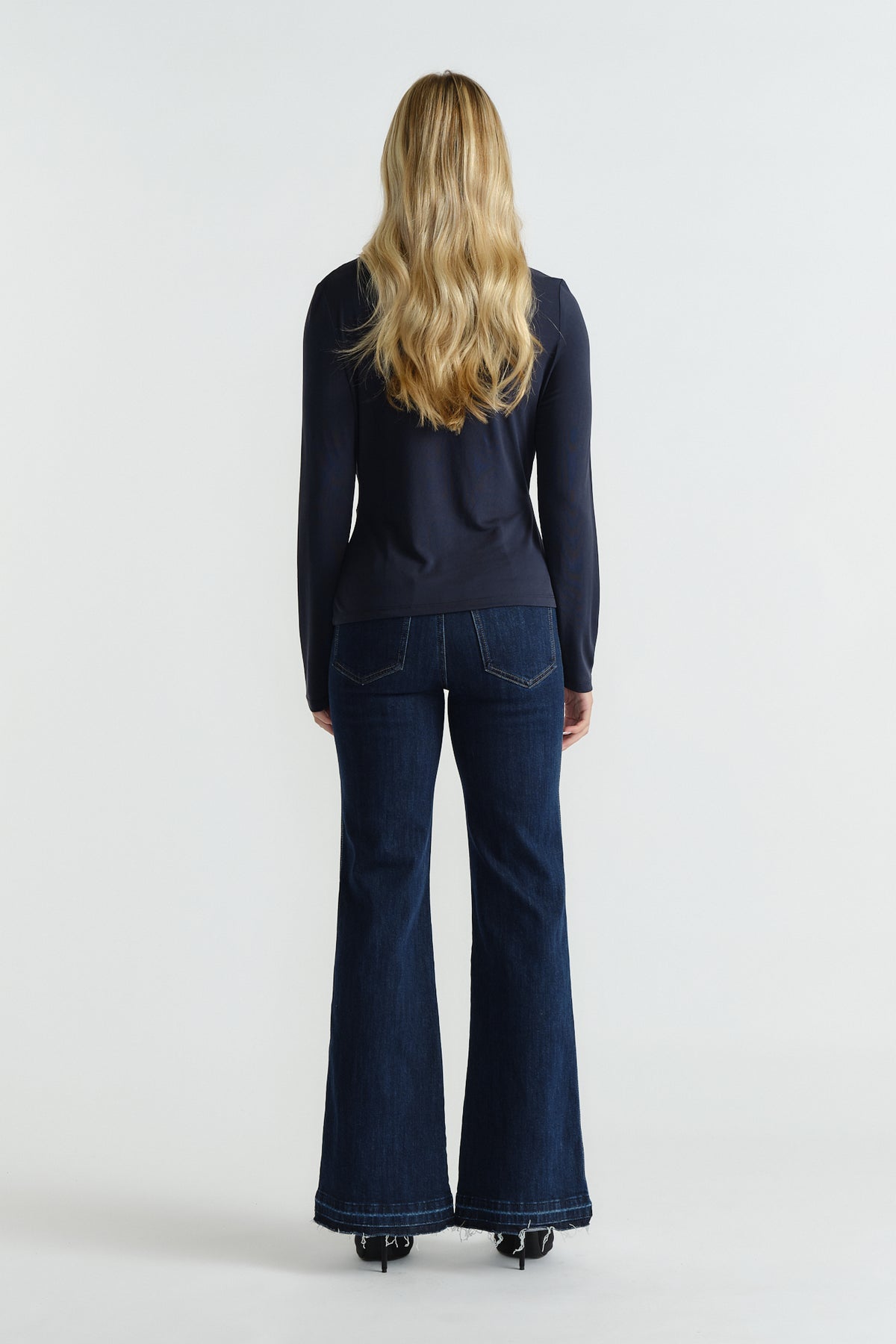 Rear view of woman wearing a navy fitted long-sleeve top paired with dark flared denim jeans and black heels