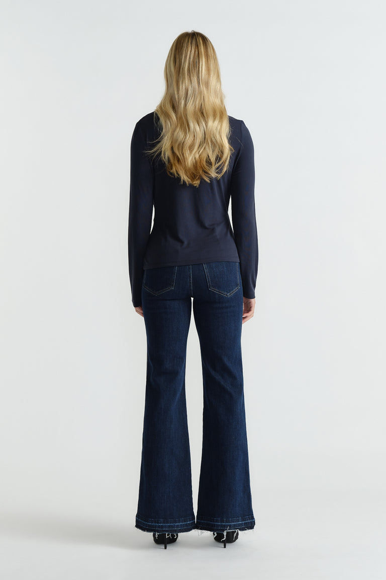 Rear view of woman wearing a navy fitted long-sleeve top paired with dark flared denim jeans and black heels