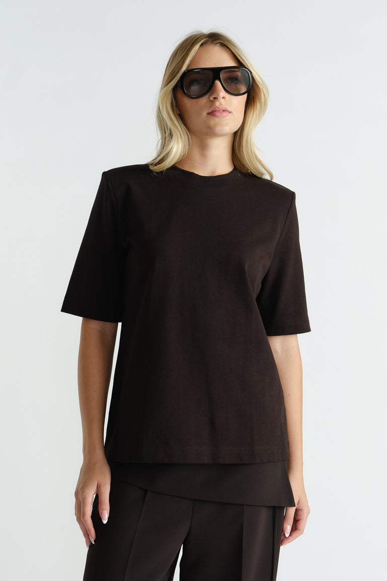 Woman wearing a black tee with structured shoulder pads paired with matching tailored pants and oversized sunglasses