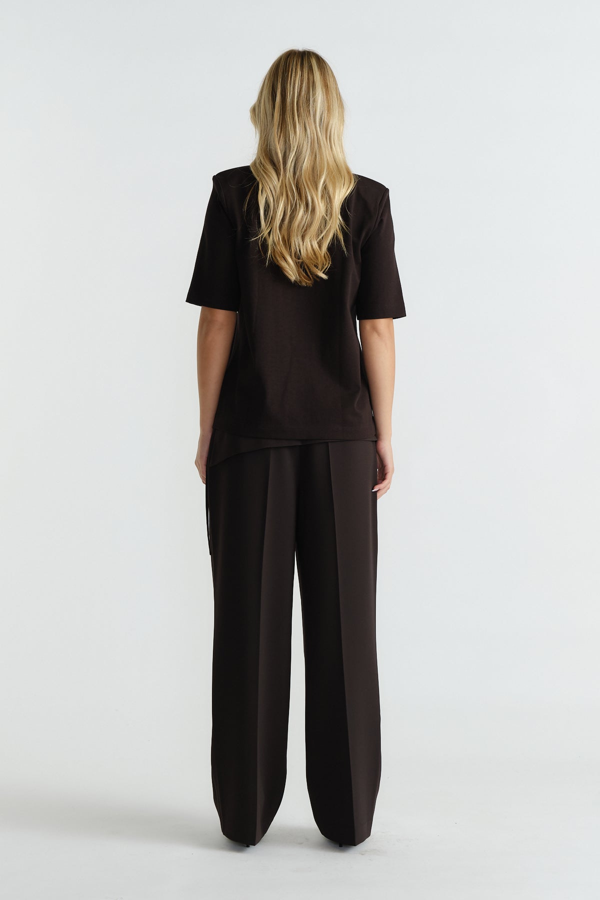 Back view of woman wearing a black shoulder pad tee paired with wide-leg tailored trousers for a polished look.