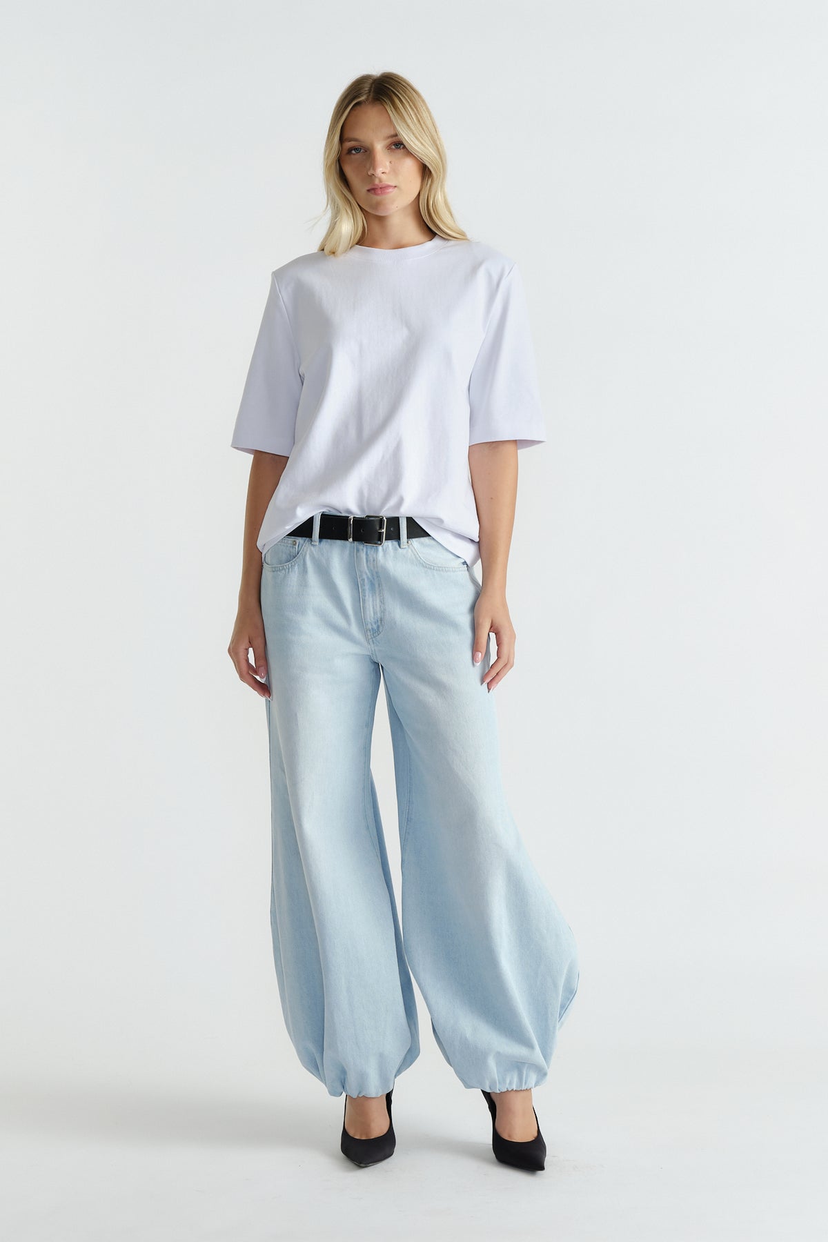 Woman wearing a relaxed white shoulder pad tee tucked into light-wash balloon jeans with black belt and heels