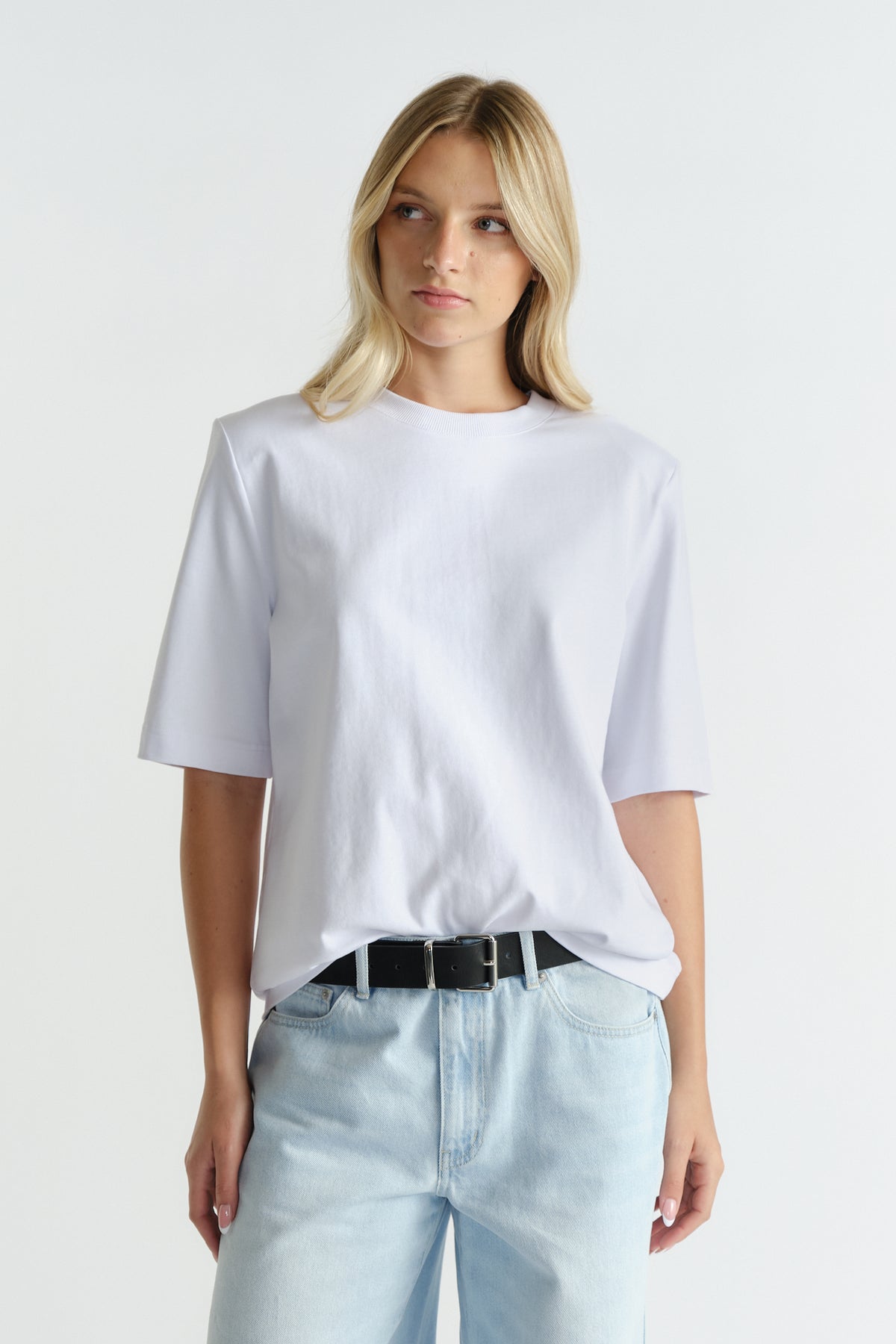 Woman wearing a bright white tee with structured shoulder pads paired with light blue relaxed-fit denim jeans and a black belt