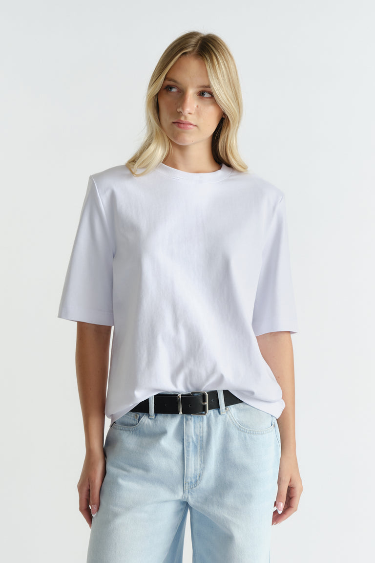 Woman wearing a bright white tee with structured shoulder pads paired with light blue relaxed-fit denim jeans and a black belt