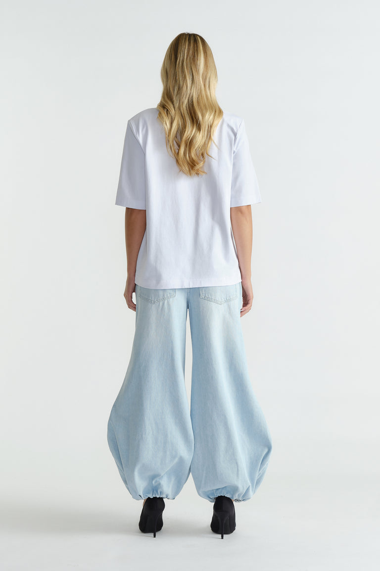 Woman wearing relaxed light blue wide-leg jeans cinched at the ankles paired with a loose white shoulder pad tee.