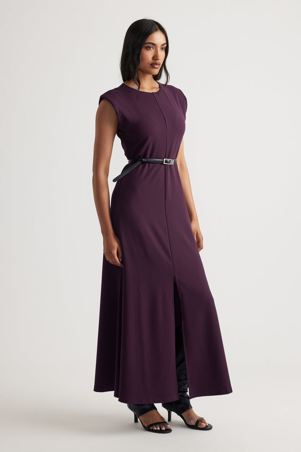 Side view of model wearing deep purple Bonnie Shoulder Pad Maxi Dress with black belt and open-toe heels by Decjuba Australian brand