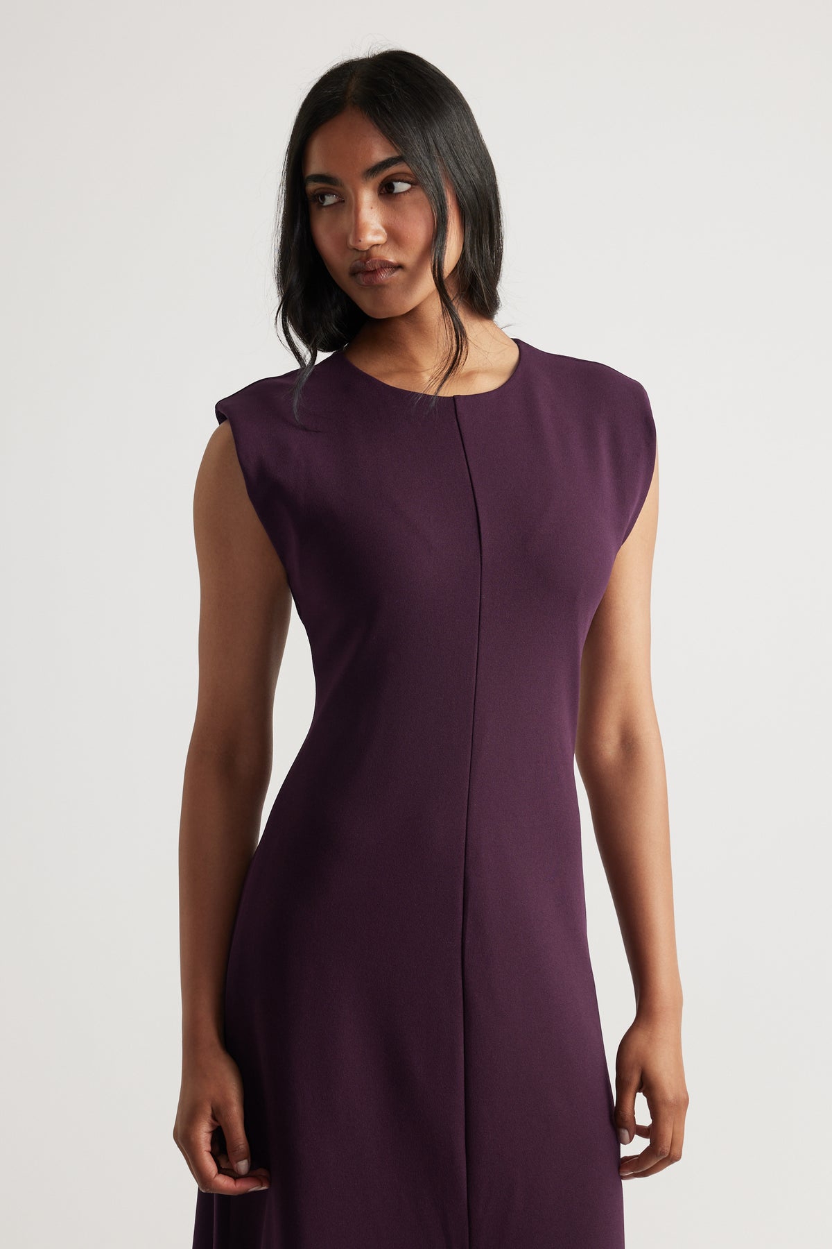 Woman wearing a sleeveless burgundy dress with subtle shoulder detailing and a central seam down the front