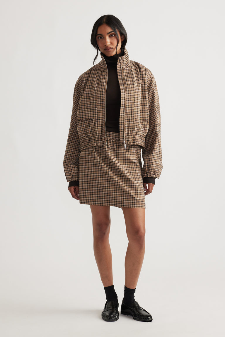 Woman wearing a checkered blazer and matching mini skirt paired with black turtleneck, socks, and loafers