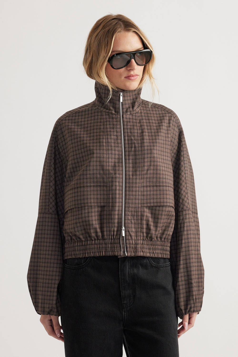 Woman wearing a high-neck checked jacket with elasticated cuffs and hem styled with black pants and sunglasses