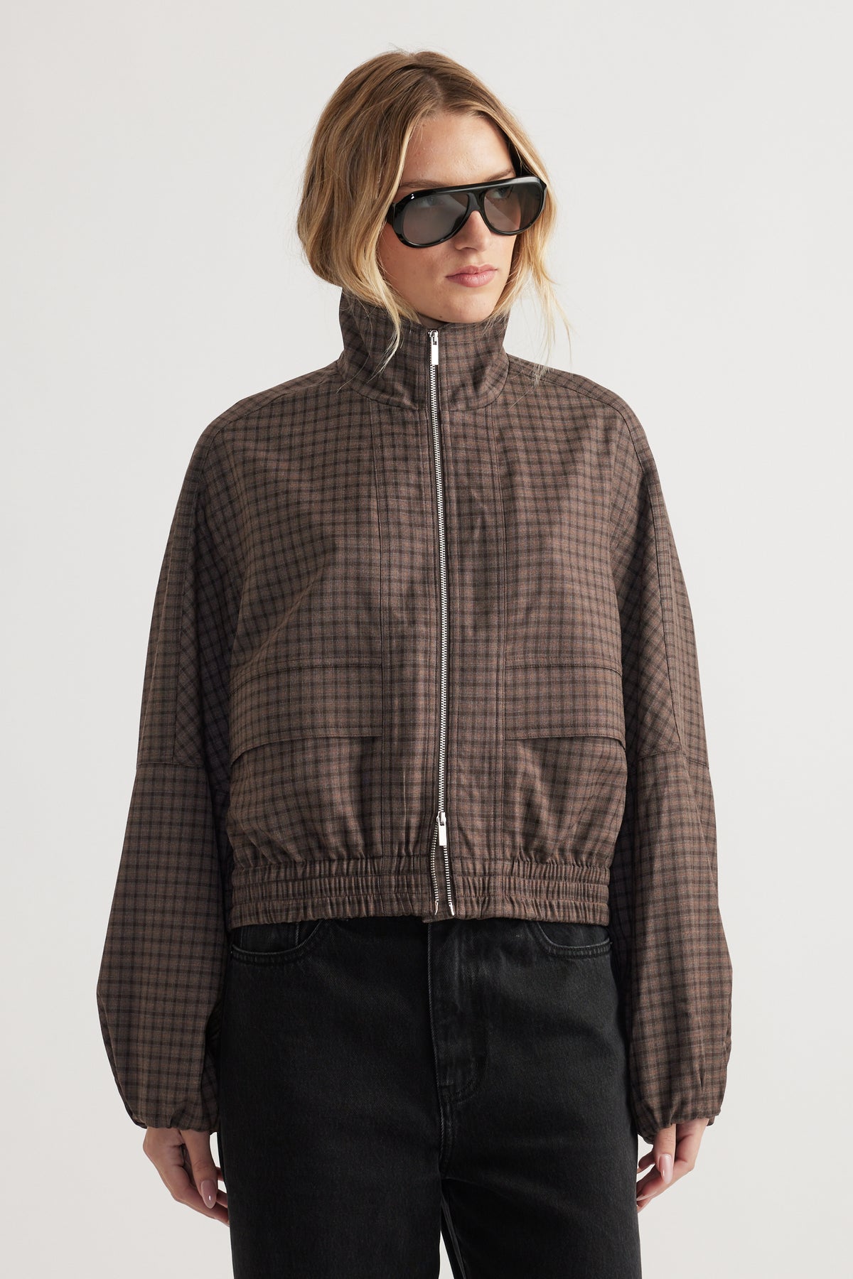 Woman wearing a high-neck checked jacket with elasticated cuffs and hem styled with black pants and sunglasses