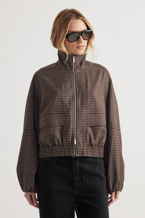 Woman wearing a high-neck checked jacket with elasticated cuffs and hem styled with black pants and sunglasses