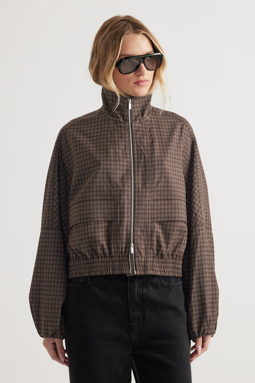 Woman wearing a high-neck checked jacket with elasticated cuffs and hem styled with black pants and sunglasses