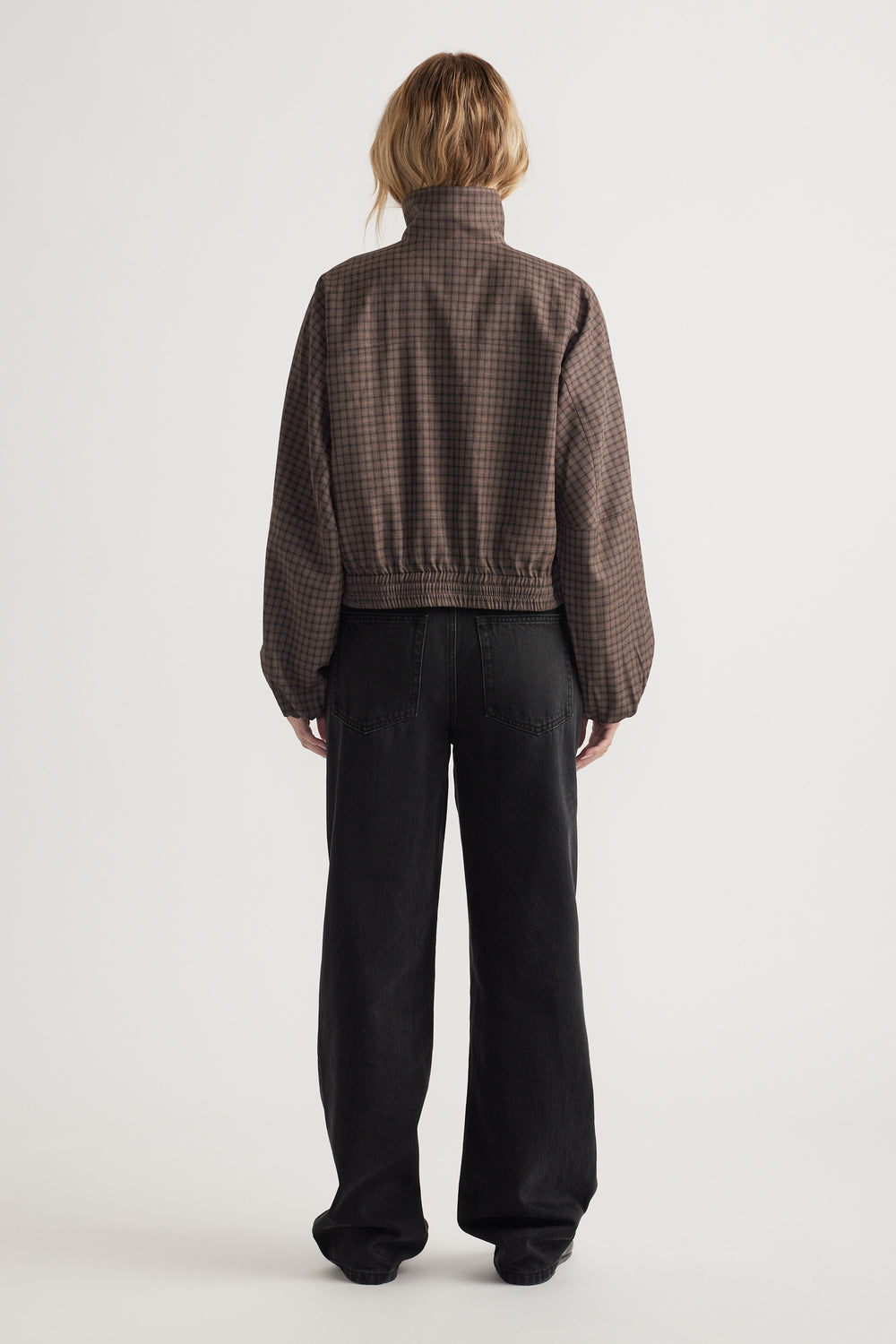 Back view of a woman wearing a cropped check jacket with elastic hem and loose black wide-leg pants