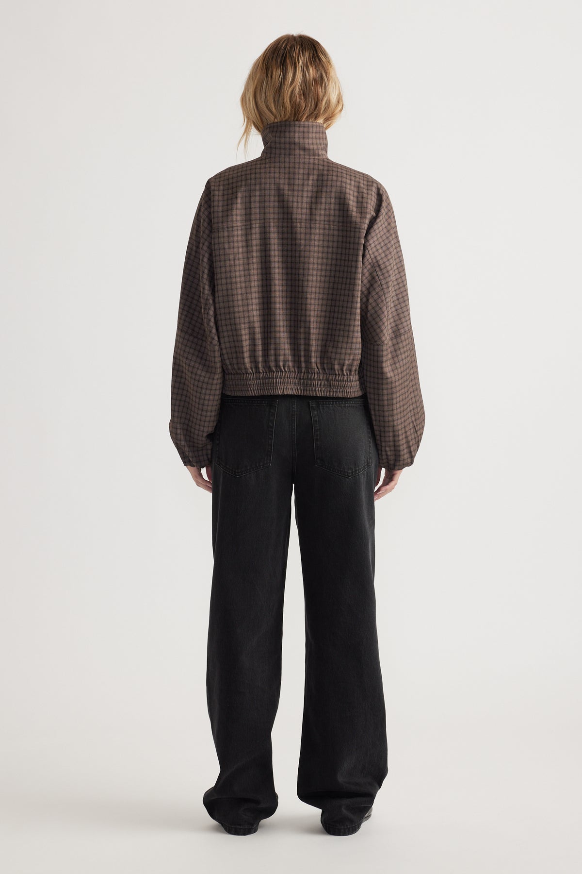 Back view of a woman wearing a cropped check jacket with elastic hem and loose black wide-leg pants