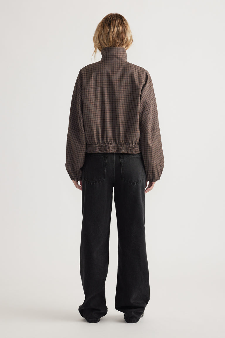 Back view of a woman wearing a cropped check jacket with elastic hem and loose black wide-leg pants