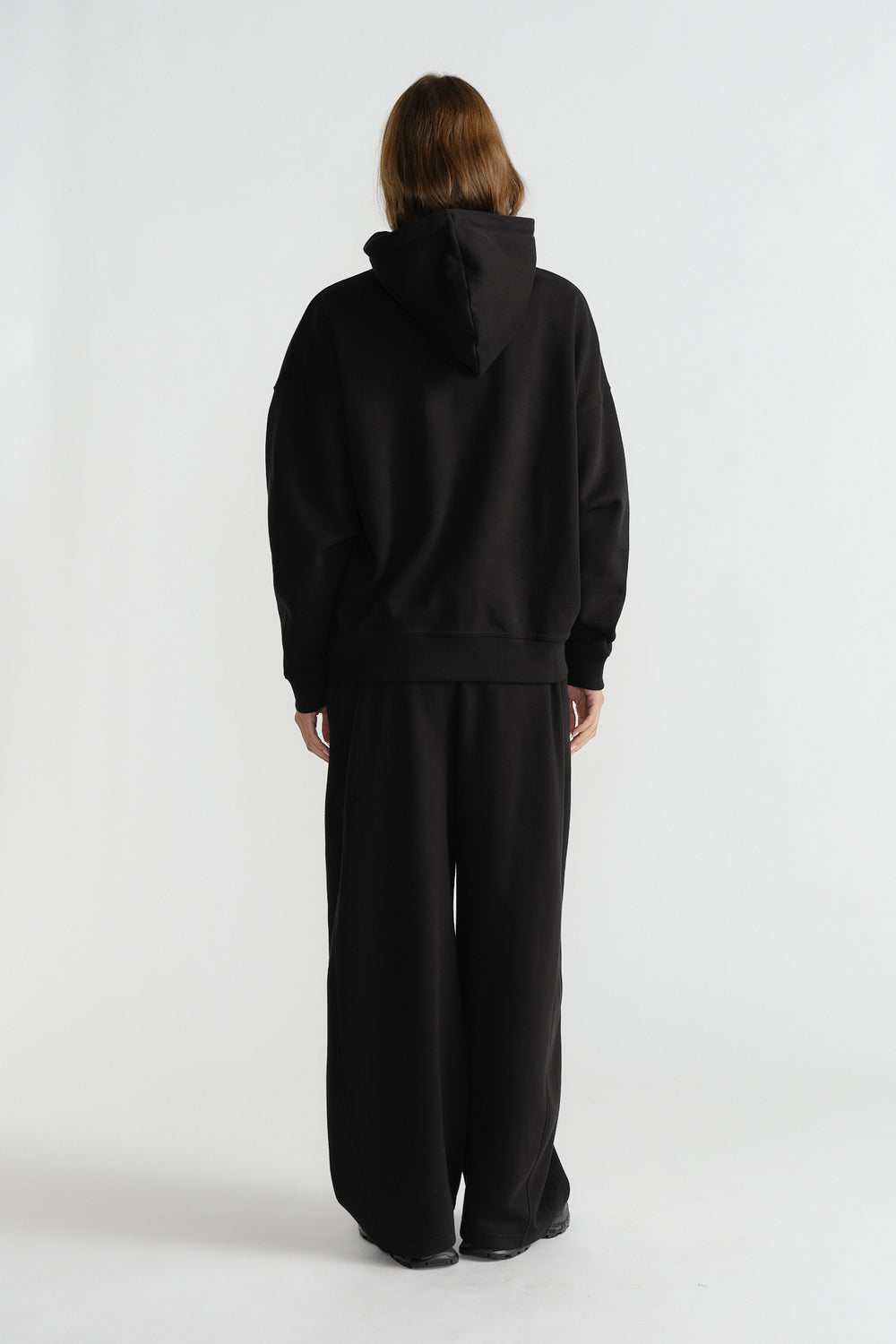 Model wearing relaxed-fit black hoodie with wide-leg black pants, styled for comfortable everyday fashion.