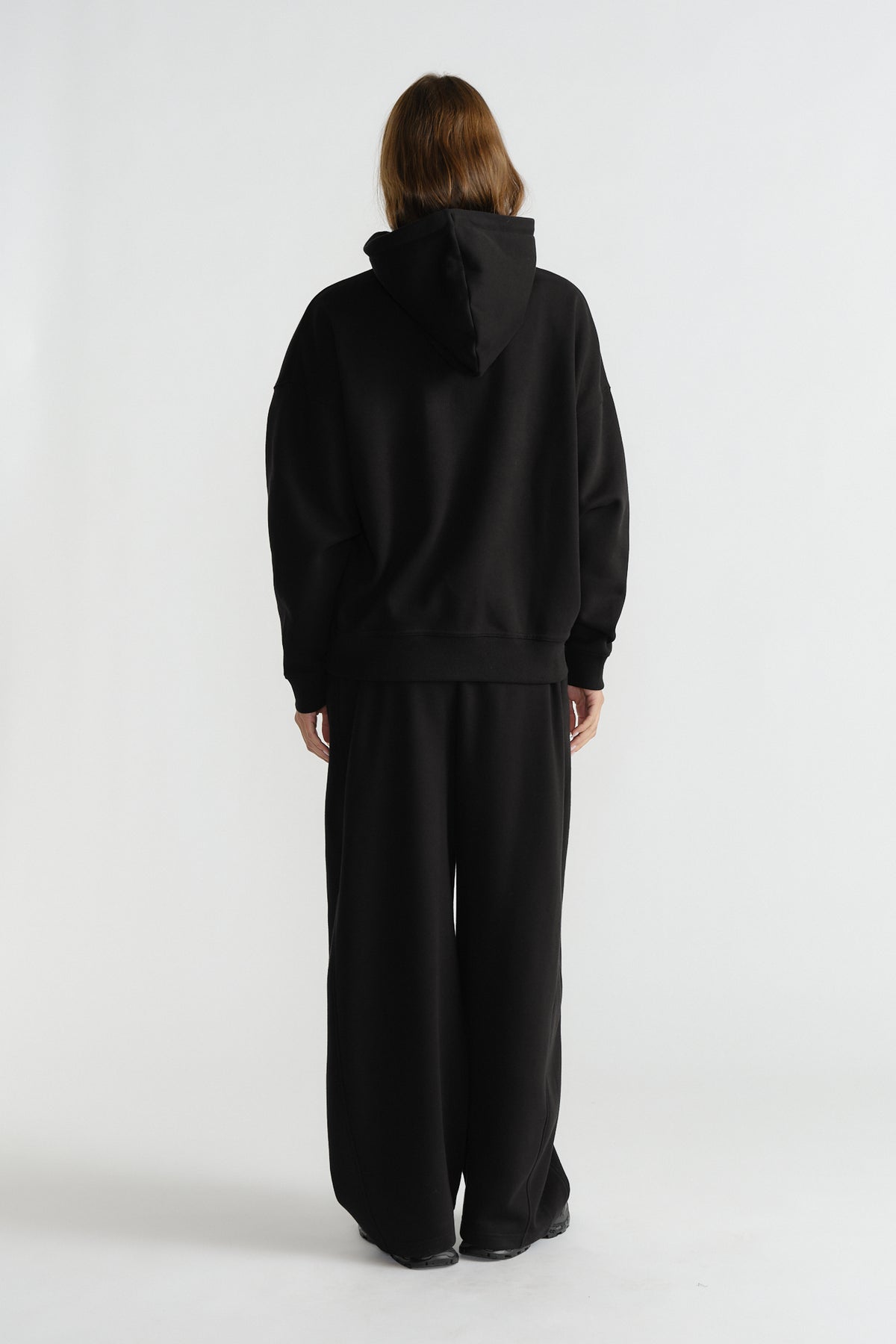 Model wearing relaxed-fit black hoodie with wide-leg black pants, styled for comfortable everyday fashion.