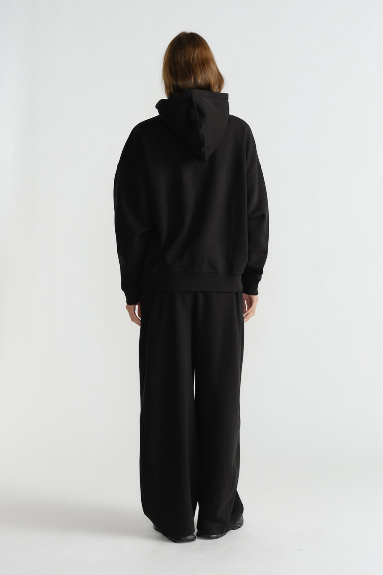 Model wearing relaxed-fit black hoodie with wide-leg black pants, styled for comfortable everyday fashion.