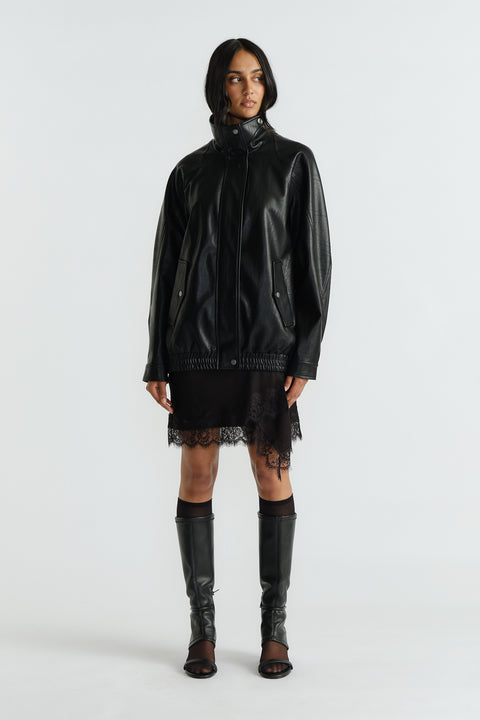 Woman wearing a black oversized jacket with high collar, paired with lace-trimmed black dress and knee-high boots