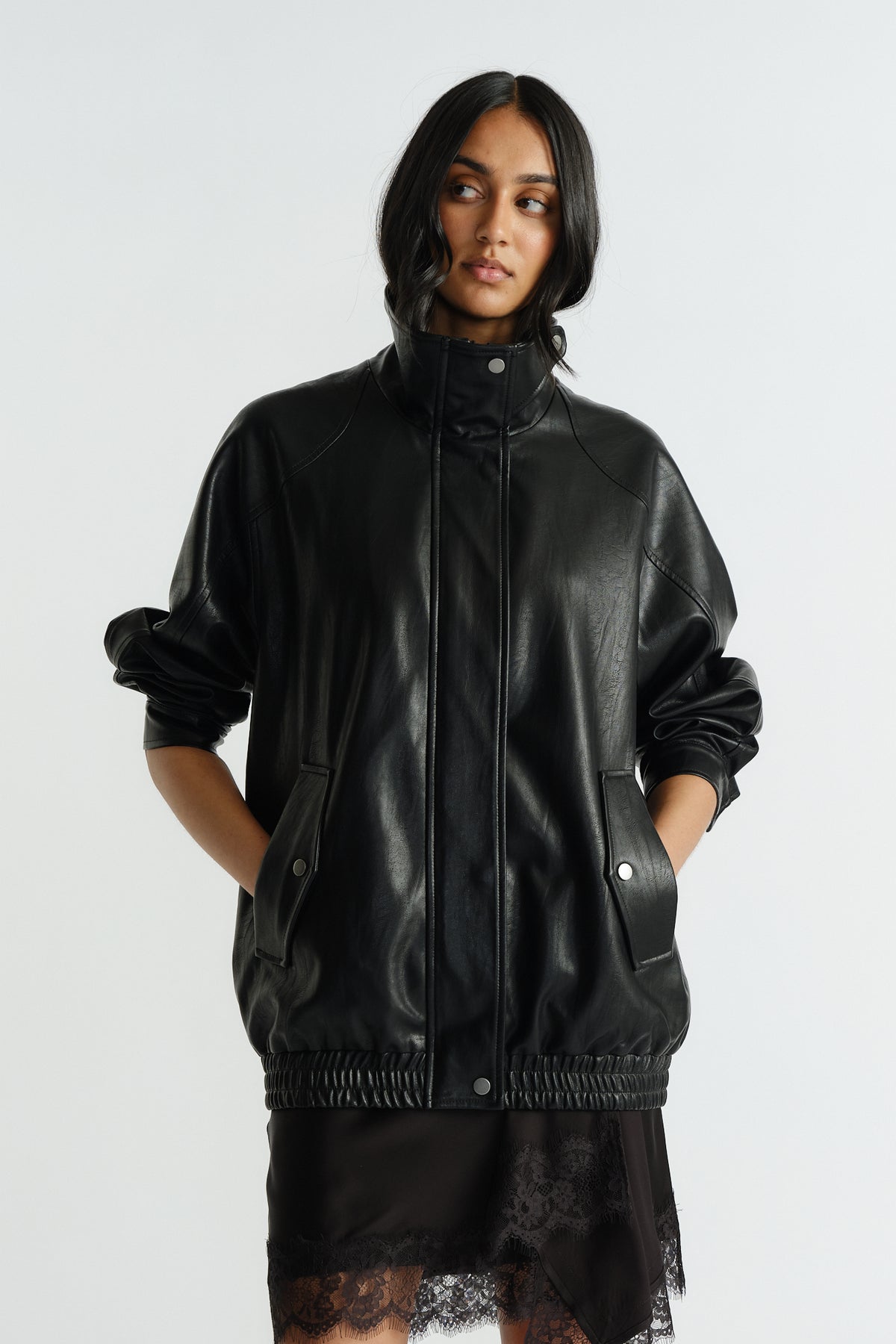 Woman wearing a relaxed-fit black oversized jacket with snap buttons, front flap pockets, and ruched hem over lace-trim skirt